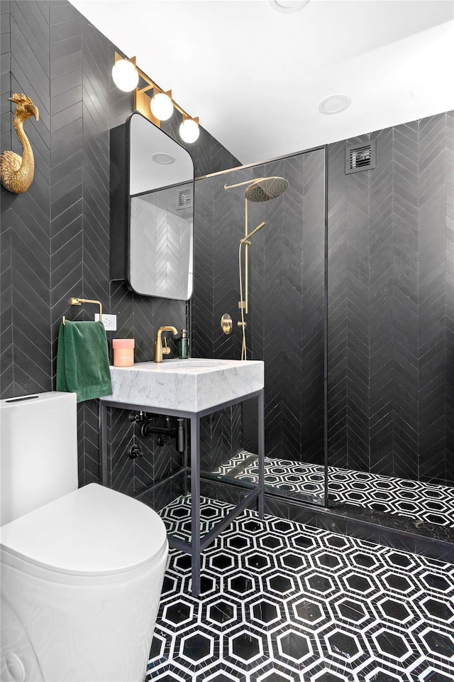 bathroom with tile walls, a walk in shower, a sink, and toilet