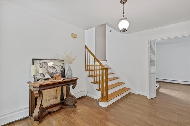 staircase with baseboard heating, wood finished floors, and baseboards