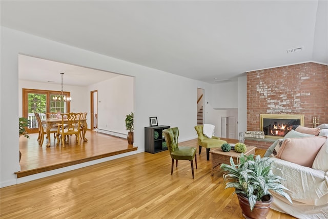 living room featuring light wood-style floors, a baseboard heating unit, stairs, a brick fireplace, and a chandelier