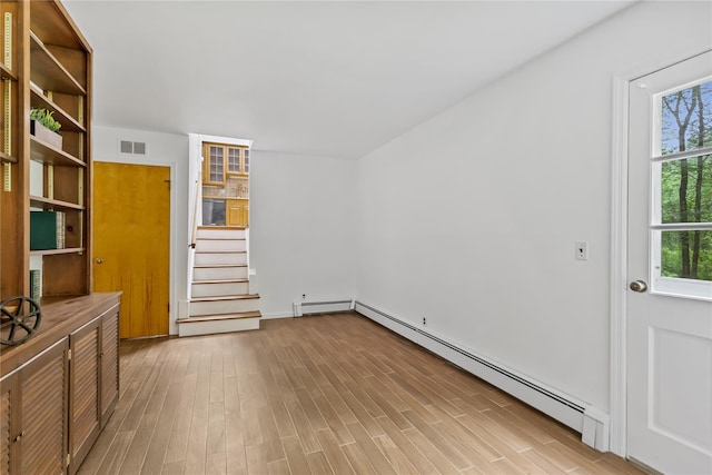 spare room with baseboard heating, wood finished floors, stairway, and baseboards