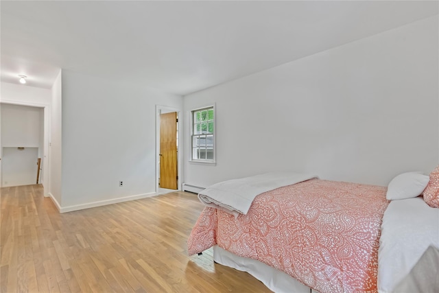 bedroom with a baseboard radiator, light wood-style floors, and baseboards
