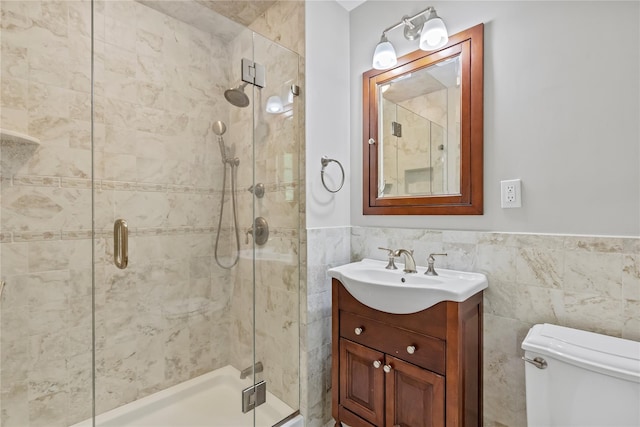 full bathroom with a stall shower, tile walls, toilet, wainscoting, and vanity