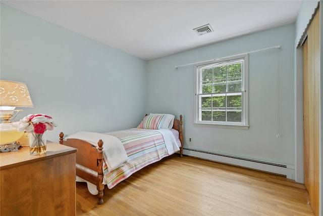 bedroom with a baseboard heating unit and light wood-type flooring