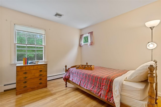 bedroom featuring a baseboard heating unit, light wood finished floors, and multiple windows