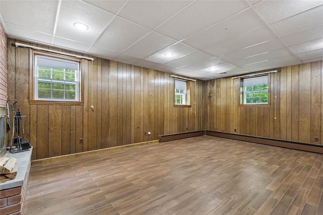 basement with wood finished floors, healthy amount of natural light, wooden walls, a paneled ceiling, and a baseboard radiator