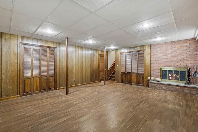 finished below grade area with wood finished floors, wood walls, stairs, a brick fireplace, and a drop ceiling