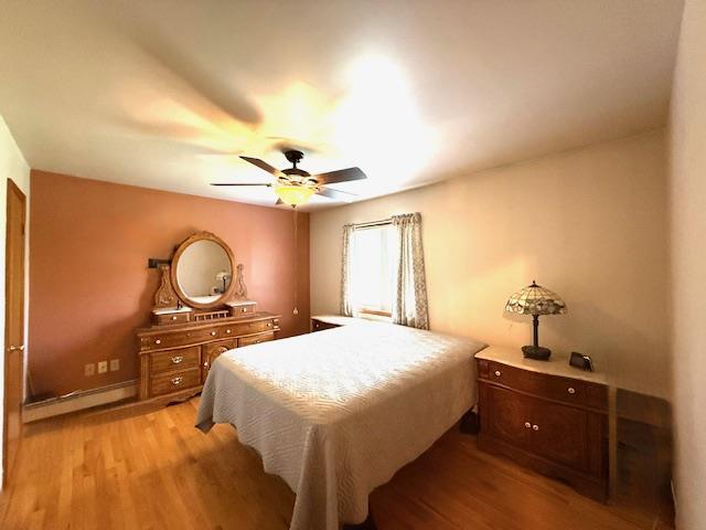 bedroom featuring light wood-style floors, baseboard heating, and ceiling fan