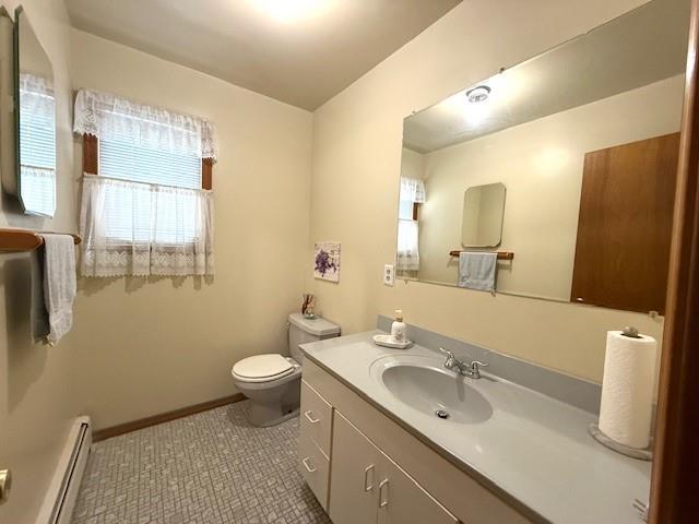 bathroom with a baseboard radiator, toilet, vanity, baseboards, and tile patterned flooring