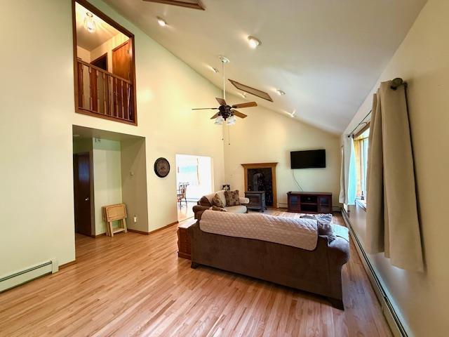 living area with a baseboard radiator, ceiling fan, light wood finished floors, high vaulted ceiling, and baseboards