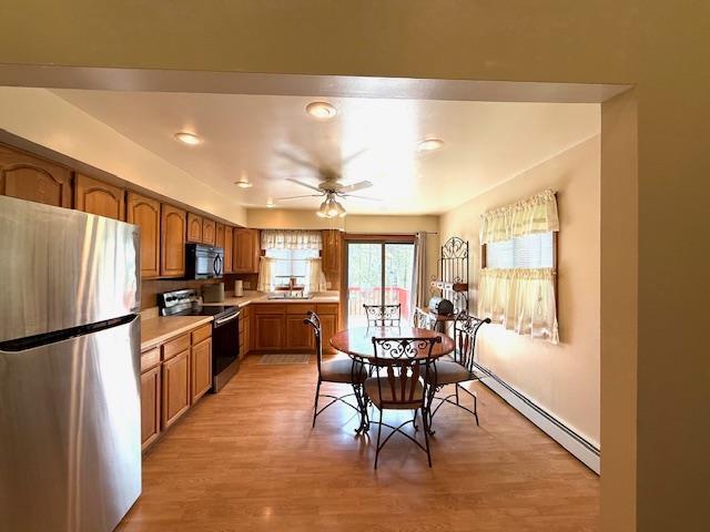 kitchen featuring freestanding refrigerator, range with electric cooktop, baseboard heating, black microwave, and brown cabinetry