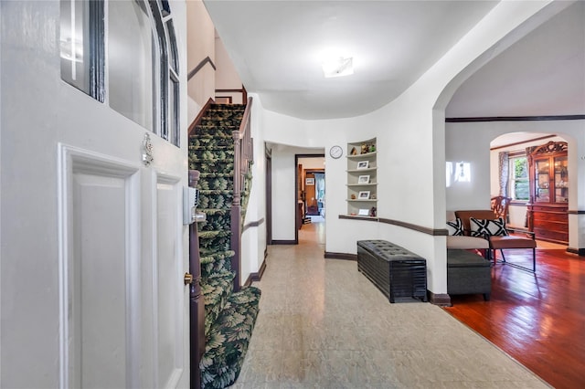 corridor with arched walkways, wood finished floors, built in features, and baseboards