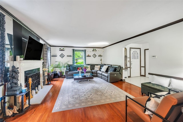 living area featuring arched walkways, wood finished floors, crown molding, and a fireplace with raised hearth