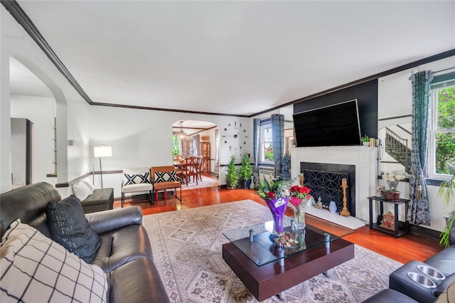 living room with ornamental molding, wood finished floors, arched walkways, and a fireplace with raised hearth