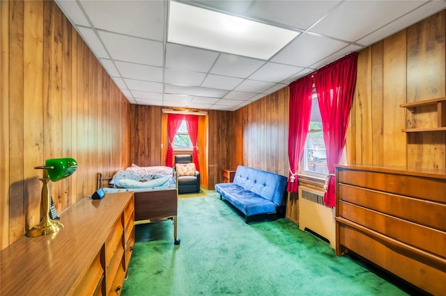 bedroom featuring carpet floors, wood walls, radiator heating unit, and a drop ceiling