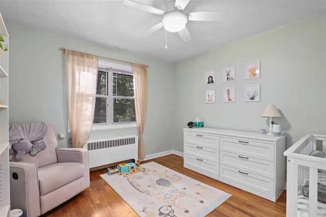 121 N Broadway Unit 22F, White Plains, NY 10603 - bedroom featuring radiator heating unit, a nursery area, light wood finished floors, and a ceiling fan