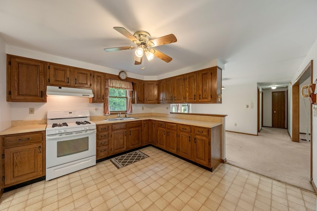 kitchen with white gas range, under cabinet range hood, light countertops, a ceiling fan, and brown cabinetry