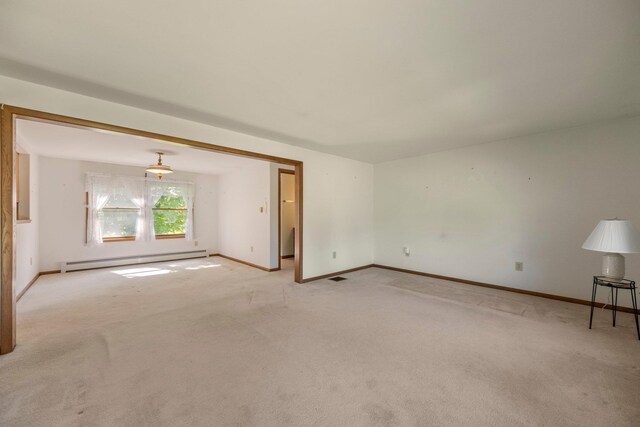 empty room featuring a baseboard heating unit, light colored carpet, and baseboards