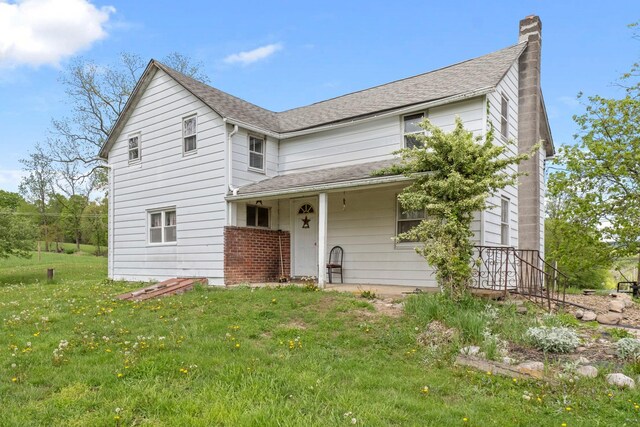 traditional-style house featuring a chimney, a front lawn, and a shingled roof