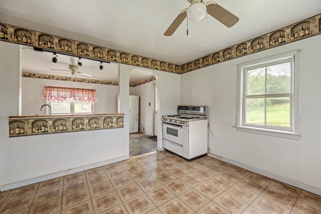 kitchen with white range with gas stovetop, a ceiling fan, arched walkways, baseboards, and a sink