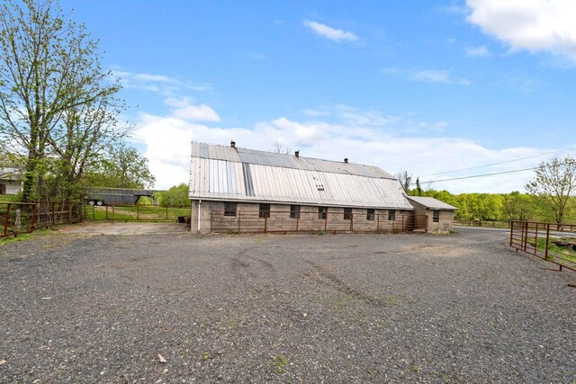 back of house with fence, metal roof, an outdoor structure, and a barn