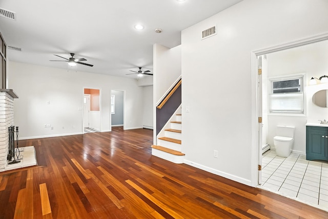 1755 Parmly Rd, Mohegan Lake, NY 10547 - unfurnished living room with ceiling fan, stairs, a brick fireplace, wood finished floors, and a baseboard radiator