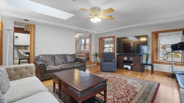 living area featuring a ceiling fan, a skylight, light wood-type flooring, and baseboards