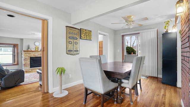 dining area featuring light wood-style floors, baseboards, a ceiling fan, and a fireplace
