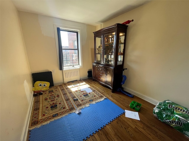 exercise room featuring radiator, wood finished floors, and baseboards