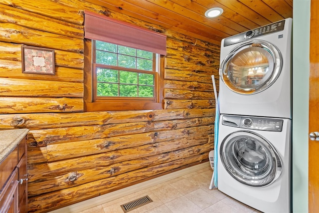 laundry area featuring stacked washer / dryer, light tile patterned flooring, wood ceiling, cabinet space, and wood walls