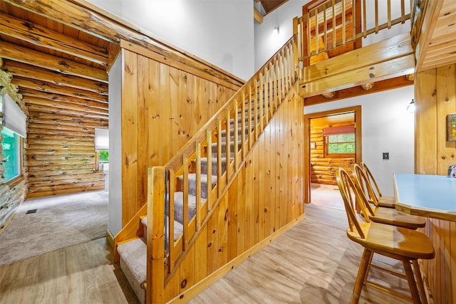 stairway with log walls, wood finished floors, and a high ceiling