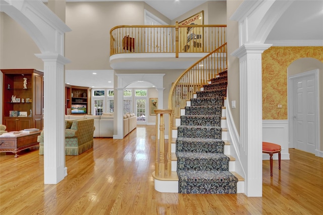 stairs with decorative columns, arched walkways, wainscoting, wood finished floors, and wallpapered walls