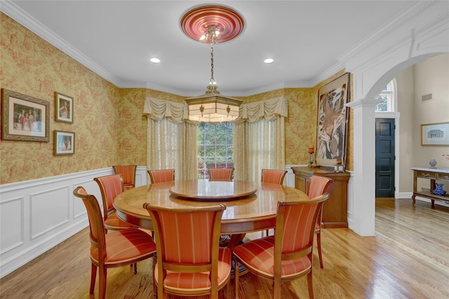 dining room with wallpapered walls, arched walkways, wainscoting, light wood-style flooring, and decorative columns