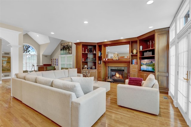 living room with ornate columns, a high end fireplace, light wood finished floors, recessed lighting, and lofted ceiling