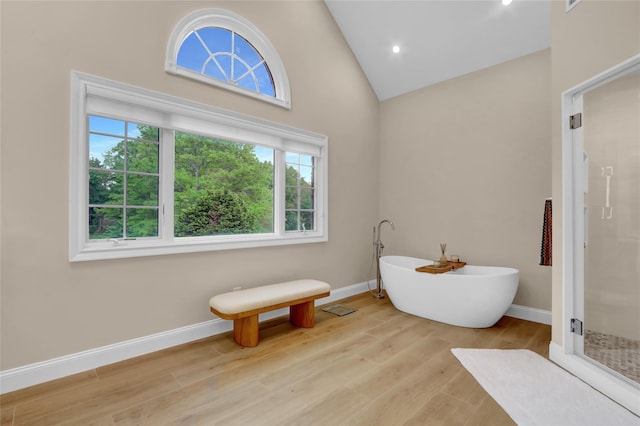 bathroom featuring a stall shower, baseboards, a soaking tub, wood finished floors, and high vaulted ceiling