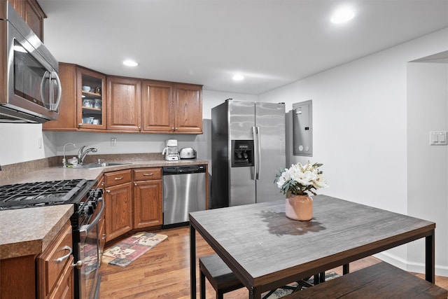 kitchen featuring appliances with stainless steel finishes, brown cabinetry, light wood-type flooring, a sink, and glass insert cabinets