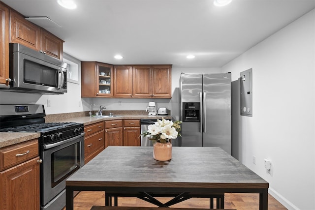 kitchen featuring appliances with stainless steel finishes, brown cabinets, a sink, glass insert cabinets, and recessed lighting