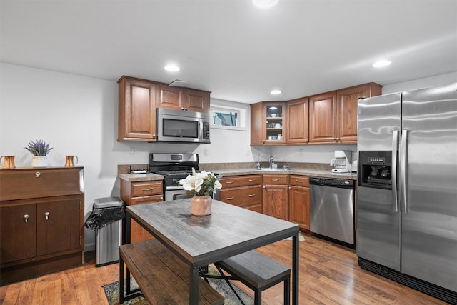 kitchen with appliances with stainless steel finishes, a sink, brown cabinetry, light wood-style floors, and glass insert cabinets