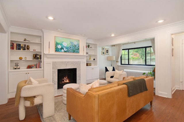 living area with ornamental molding, wood finished floors, radiator heating unit, a premium fireplace, and baseboards