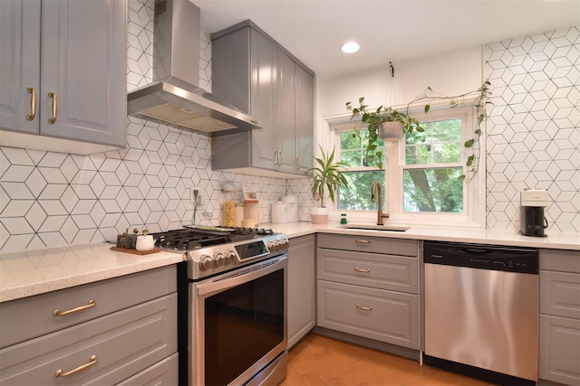 kitchen featuring appliances with stainless steel finishes, gray cabinetry, wall chimney range hood, a sink, and backsplash