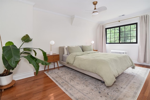 bedroom featuring radiator, wood finished floors, ornamental molding, baseboards, and a ceiling fan