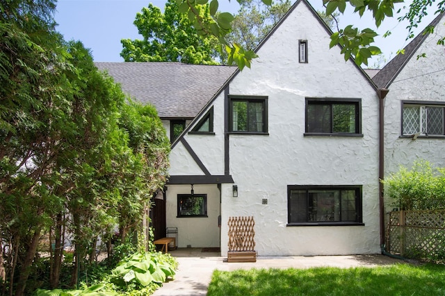 rear view of house featuring stucco siding, roof with shingles, and fence