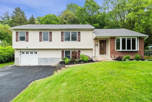 tri-level home featuring asphalt driveway, a front yard, an attached garage, and view of scattered trees