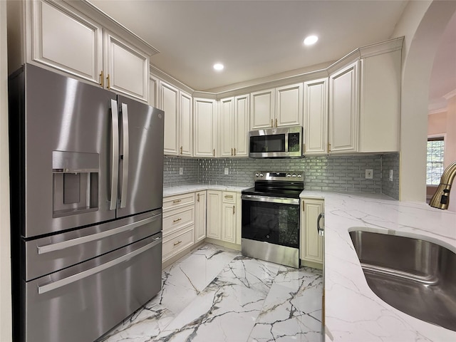 kitchen featuring appliances with stainless steel finishes, a sink, recessed lighting, arched walkways, and light marble finish flooring