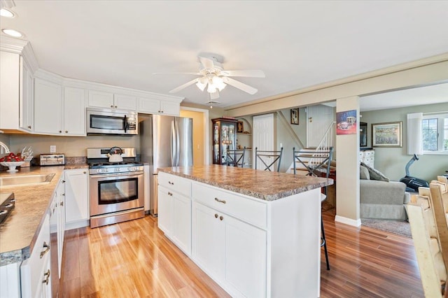 kitchen featuring appliances with stainless steel finishes, a sink, light wood-style floors, a kitchen island, and a ceiling fan