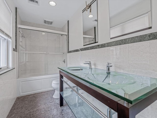 12 Pleasant Ave, Port Washington, NY 11050 - bathroom featuring tile walls, toilet, combined bath / shower with glass door, double vanity, and wainscoting