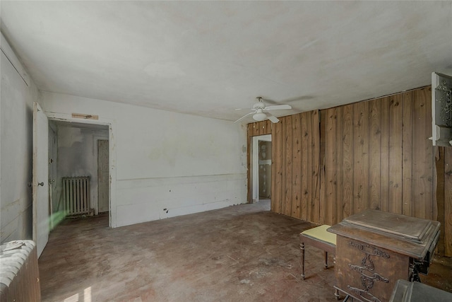 empty room featuring radiator heating unit, wooden walls, and ceiling fan