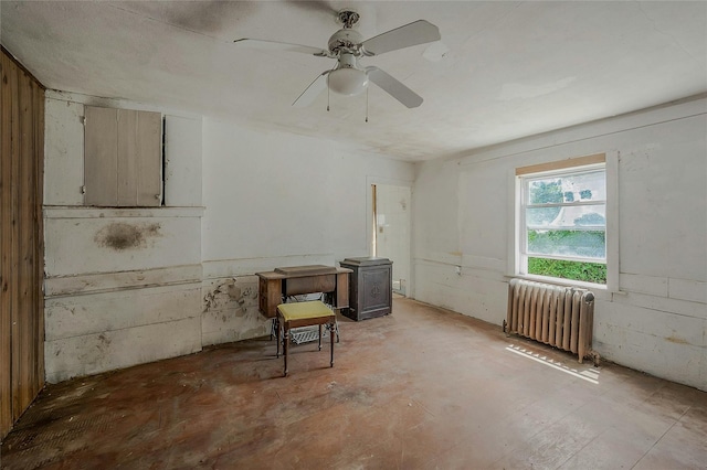 unfurnished room featuring radiator, a wood stove, and ceiling fan