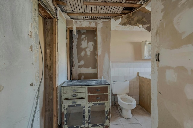 bathroom with tile patterned flooring, toilet, tile walls, and a wainscoted wall