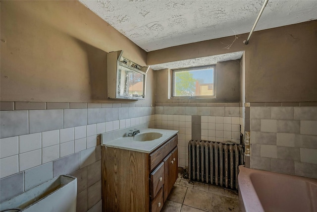 full bath with radiator, tile walls, a bathtub, vanity, and wainscoting