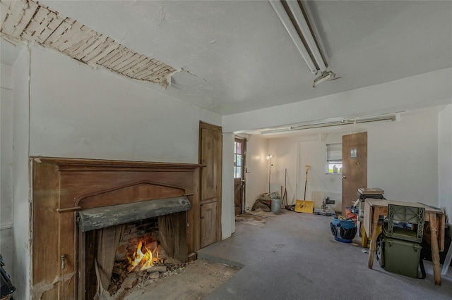 living area featuring a warm lit fireplace, plenty of natural light, and unfinished concrete flooring